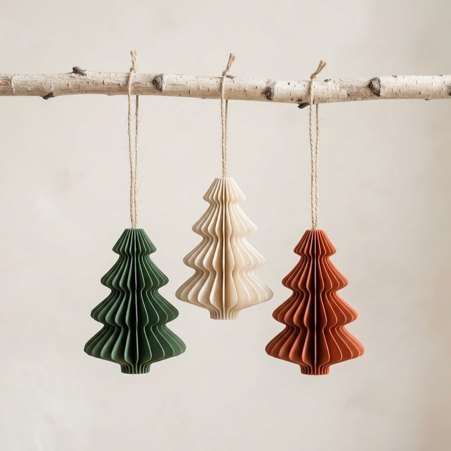 Three folded tree ornaments in forest green, bone and clay hanging from a birch branch
